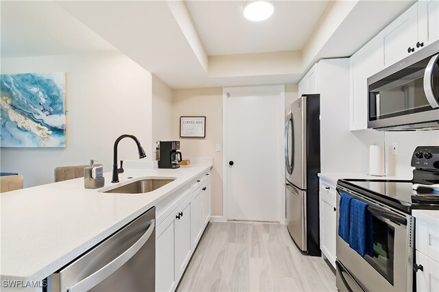 kitchen featuring kitchen peninsula, white cabinets, appliances with stainless steel finishes, light wood-type flooring, and sink