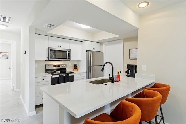 kitchen with stainless steel appliances, a sink, a breakfast bar, baseboards, and a peninsula