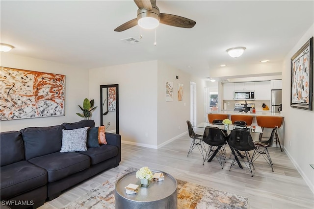 living area featuring a ceiling fan, baseboards, and light wood finished floors