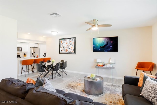living area featuring light wood-style floors, baseboards, and a ceiling fan