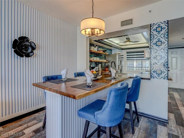 bar featuring wooden counters, wood-type flooring, ceiling fan, a raised ceiling, and decorative light fixtures