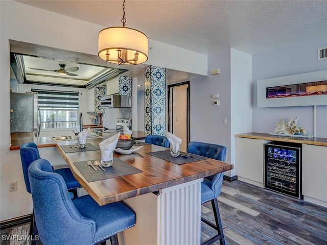 dining area with indoor wet bar, ceiling fan, dark hardwood / wood-style floors, a textured ceiling, and beverage cooler