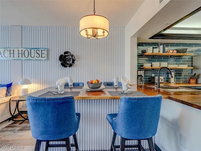 interior space with wooden counters, light wood-type flooring, hanging light fixtures, and backsplash