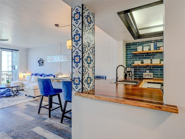 bar featuring tasteful backsplash, wooden counters, a textured ceiling, sink, and hardwood / wood-style flooring