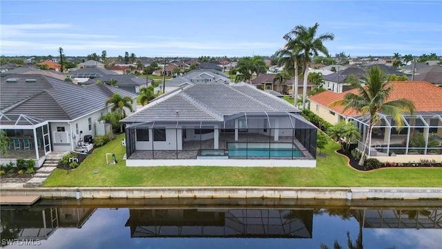 back of property with a water view, a lanai, and a lawn