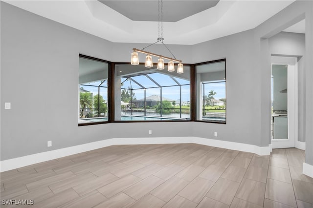 spare room with a tray ceiling and an inviting chandelier