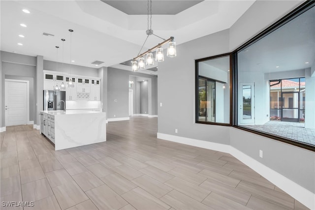 kitchen with a kitchen island with sink, light hardwood / wood-style flooring, stainless steel fridge with ice dispenser, pendant lighting, and white cabinetry