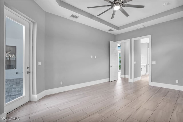 empty room featuring ceiling fan, a raised ceiling, and plenty of natural light