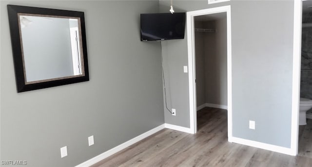 unfurnished bedroom with connected bathroom, a closet, a walk in closet, and light hardwood / wood-style floors