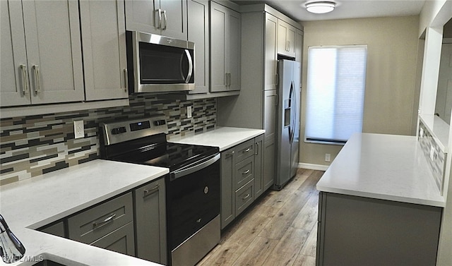 kitchen featuring gray cabinets, decorative backsplash, light hardwood / wood-style flooring, and stainless steel appliances