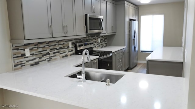 kitchen with sink, backsplash, kitchen peninsula, stainless steel appliances, and gray cabinets