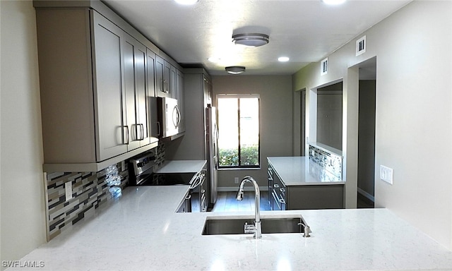 kitchen featuring light stone countertops, appliances with stainless steel finishes, sink, decorative backsplash, and light hardwood / wood-style flooring