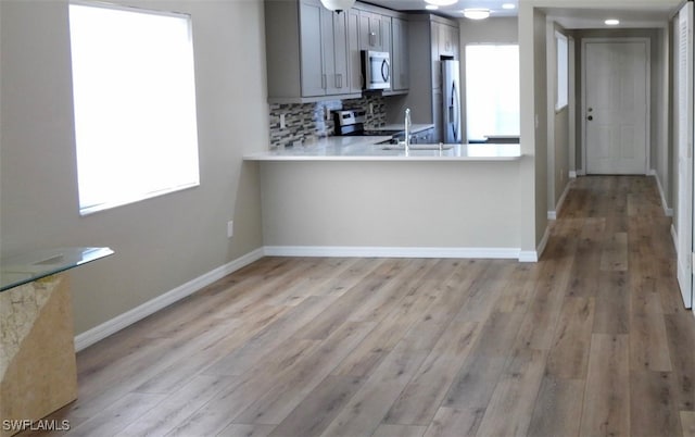 kitchen featuring backsplash, appliances with stainless steel finishes, light wood-type flooring, gray cabinets, and sink