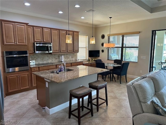 kitchen with light stone counters, hanging light fixtures, a center island with sink, appliances with stainless steel finishes, and a kitchen breakfast bar