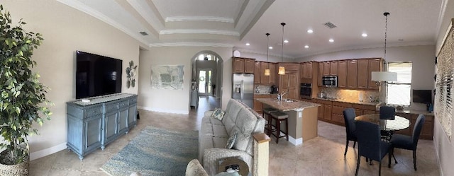 kitchen featuring appliances with stainless steel finishes, hanging light fixtures, ornamental molding, decorative backsplash, and a large island with sink