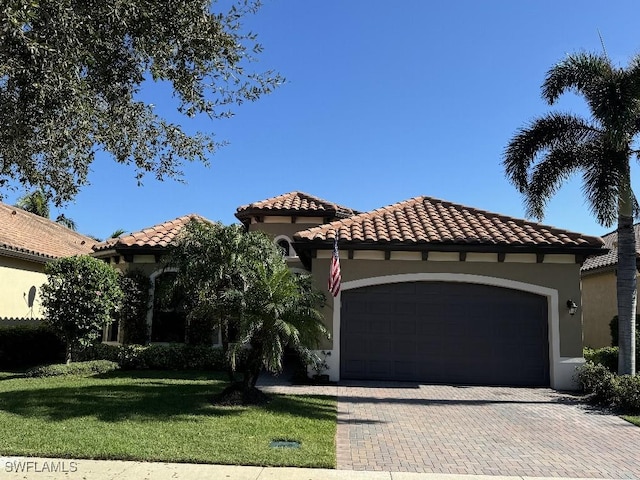 mediterranean / spanish house with a tiled roof, a front yard, stucco siding, decorative driveway, and an attached garage