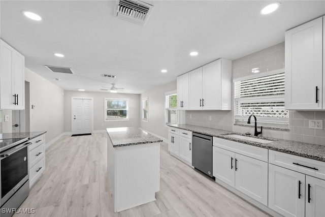 kitchen with stainless steel appliances, a sink, a kitchen island, backsplash, and light wood-style floors