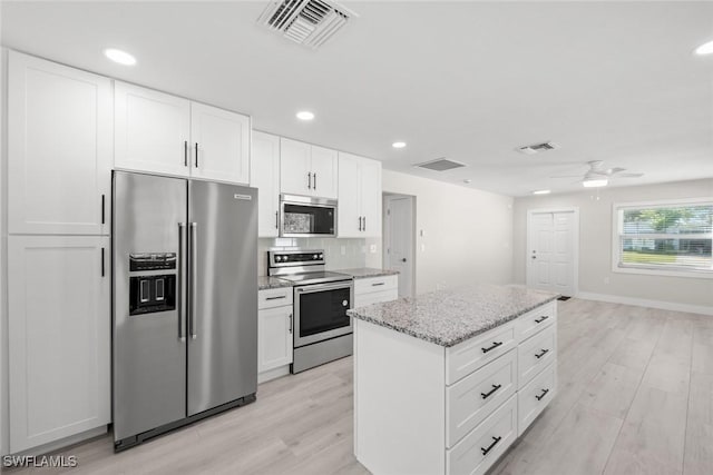 kitchen featuring appliances with stainless steel finishes, light wood-style flooring, ceiling fan, a kitchen island, and white cabinets