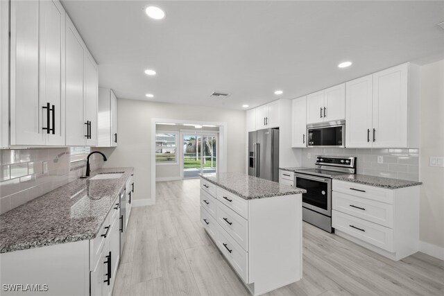 kitchen featuring stainless steel appliances, white cabinetry, sink, light stone countertops, and light wood-type flooring