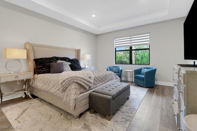 bedroom with a tray ceiling, recessed lighting, baseboards, and wood finished floors