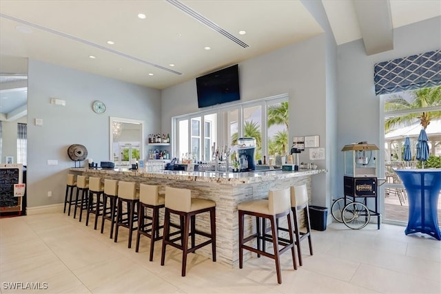 kitchen featuring a breakfast bar, light stone countertops, kitchen peninsula, and a towering ceiling