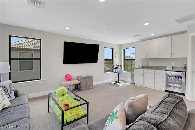 carpeted living room featuring wine cooler, indoor wet bar, visible vents, a sink, and baseboards