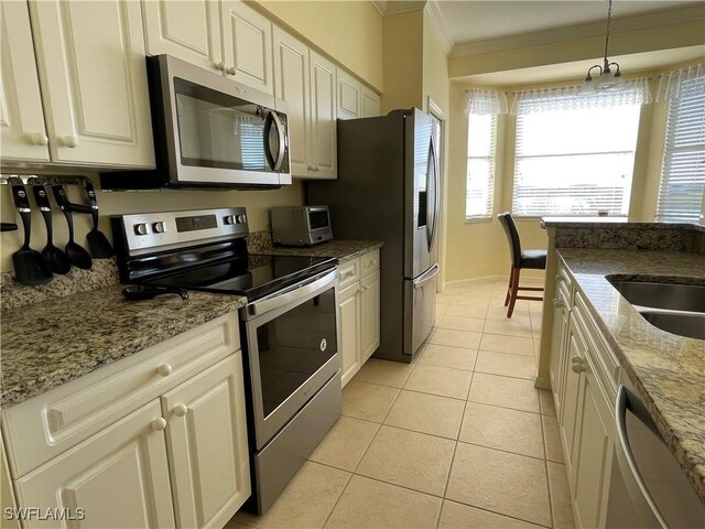 kitchen with light stone countertops, appliances with stainless steel finishes, pendant lighting, light tile patterned floors, and ornamental molding