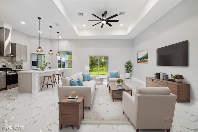 living room with a raised ceiling, ceiling fan, and a high ceiling