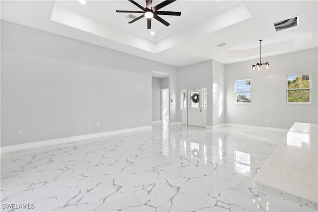 unfurnished living room with ceiling fan with notable chandelier and a tray ceiling