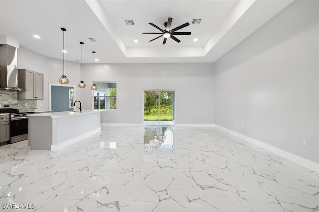 kitchen featuring gray cabinetry, an island with sink, stainless steel stove, ceiling fan, and wall chimney range hood