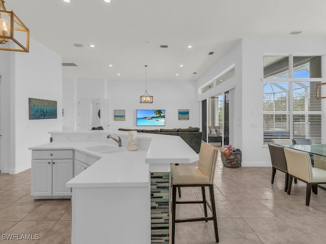 kitchen featuring a center island with sink, sink, white cabinets, and decorative light fixtures