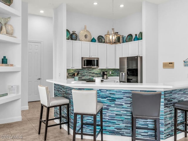 kitchen featuring kitchen peninsula, backsplash, appliances with stainless steel finishes, a kitchen breakfast bar, and white cabinetry