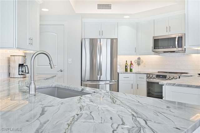 kitchen featuring backsplash, appliances with stainless steel finishes, white cabinetry, light stone countertops, and sink