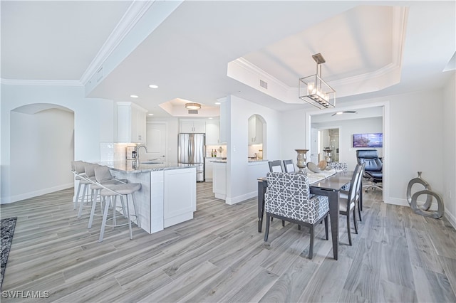 dining room with light hardwood / wood-style flooring, ornamental molding, sink, a notable chandelier, and a raised ceiling