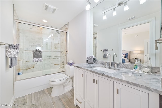 full bathroom featuring vanity, bath / shower combo with glass door, hardwood / wood-style flooring, and toilet