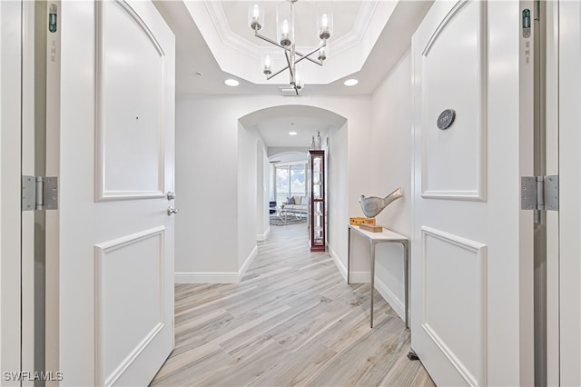 hallway with ornamental molding, a tray ceiling, and light wood-type flooring