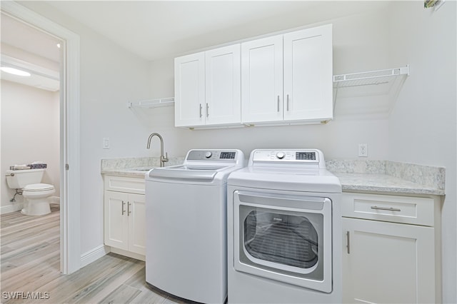 clothes washing area featuring cabinets, sink, washer and clothes dryer, and light wood-type flooring