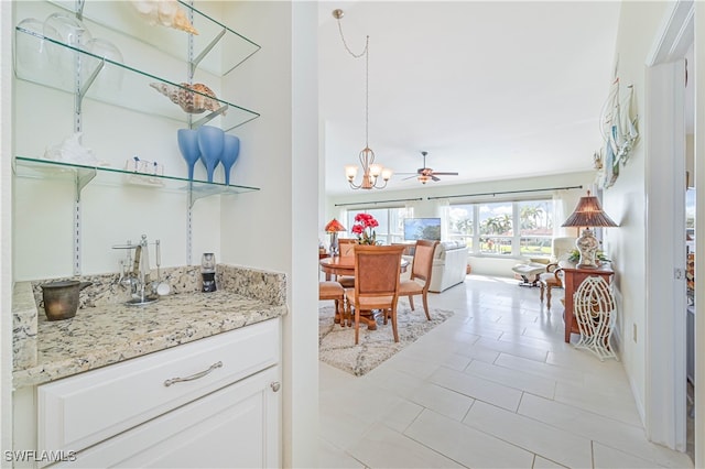 kitchen with decorative light fixtures, light tile patterned floors, white cabinets, light stone counters, and ceiling fan