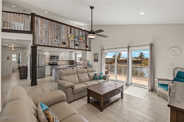 living room featuring ceiling fan, light hardwood / wood-style floors, sink, and high vaulted ceiling