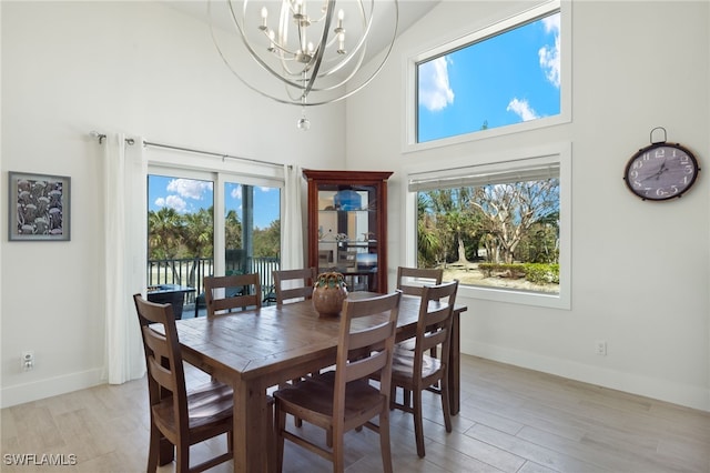 dining area with a notable chandelier, light wood-type flooring, a towering ceiling, and plenty of natural light