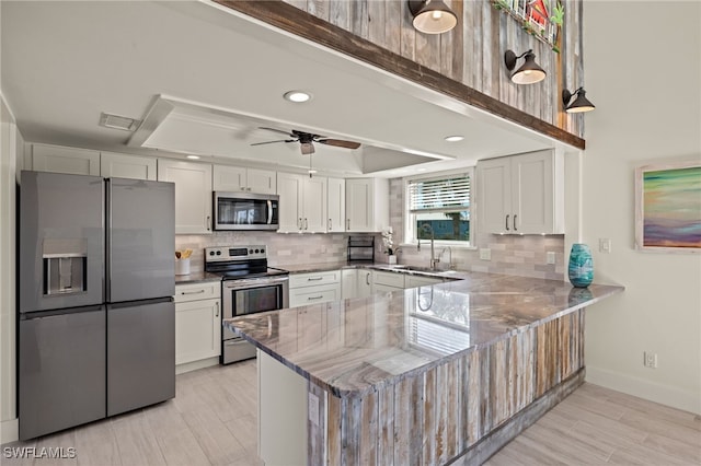 kitchen featuring kitchen peninsula, appliances with stainless steel finishes, a raised ceiling, sink, and white cabinetry