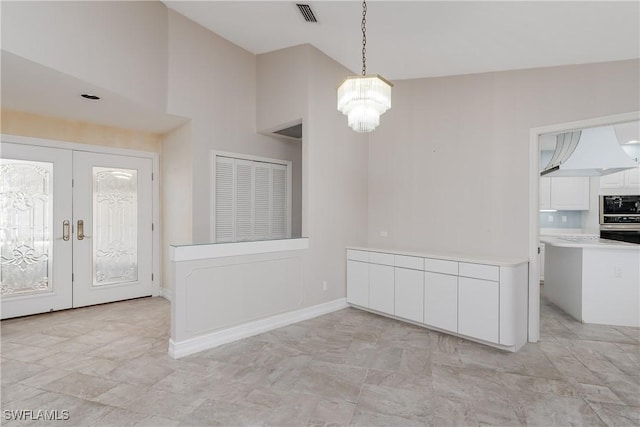 unfurnished dining area featuring a chandelier, lofted ceiling, and french doors