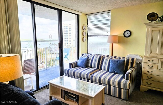 living room with a water view, light colored carpet, floor to ceiling windows, and a textured ceiling