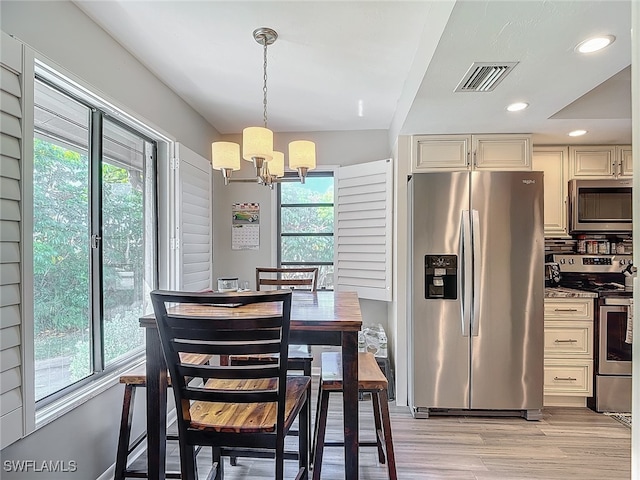 kitchen with stainless steel appliances, light hardwood / wood-style floors, tasteful backsplash, decorative light fixtures, and a notable chandelier