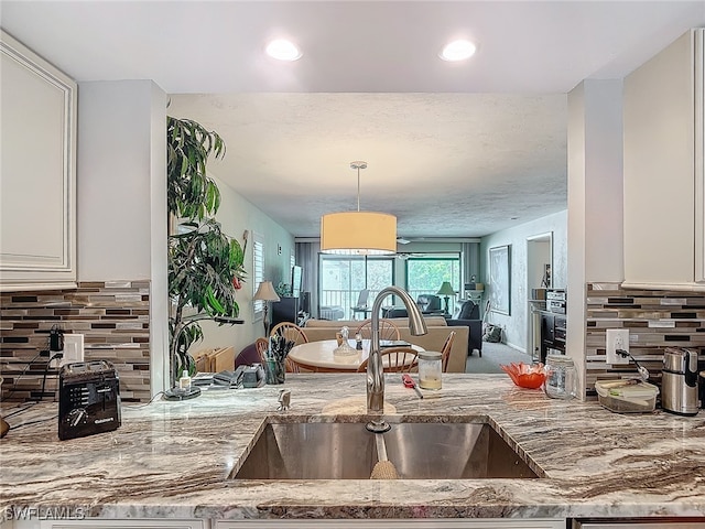 kitchen featuring white cabinetry, sink, light stone counters, tasteful backsplash, and decorative light fixtures