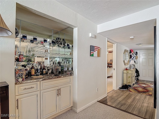 bar with cream cabinets, light hardwood / wood-style floors, and a textured ceiling