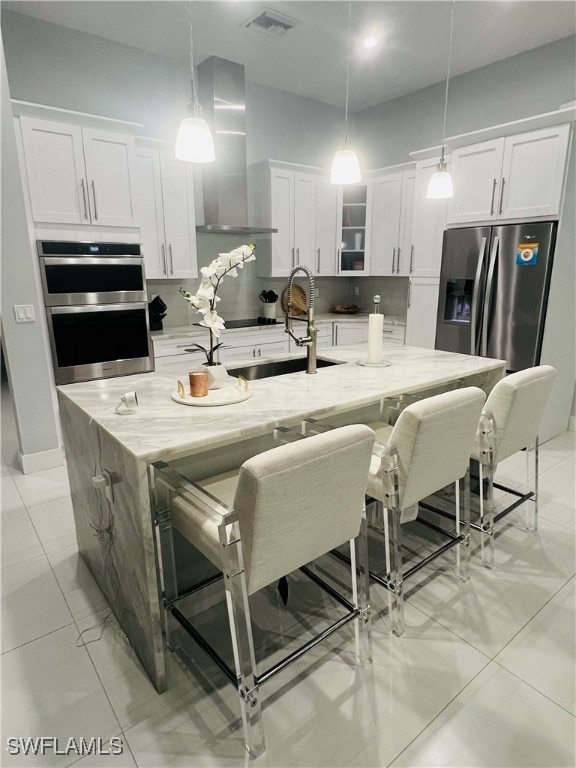 kitchen featuring a spacious island, light stone countertops, wall chimney exhaust hood, and hanging light fixtures