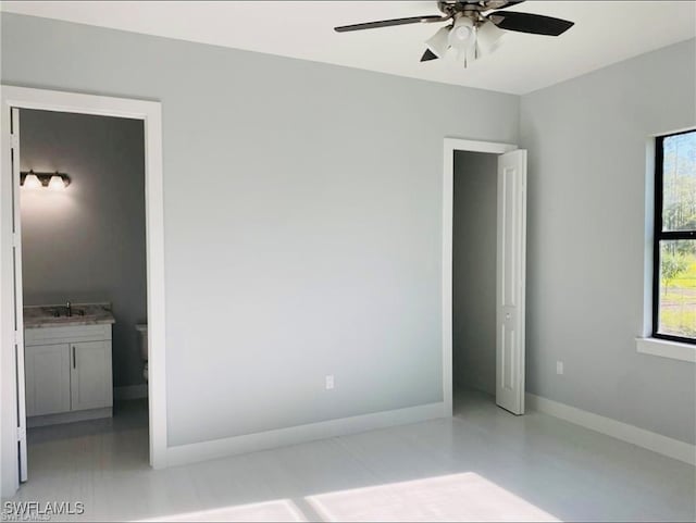 unfurnished bedroom featuring multiple windows, ensuite bathroom, sink, and ceiling fan