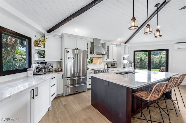 kitchen featuring light stone countertops, appliances with stainless steel finishes, a kitchen breakfast bar, wall chimney range hood, and white cabinets