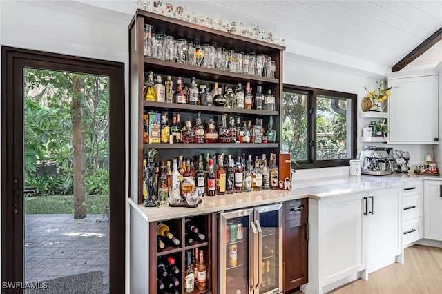 bar featuring beam ceiling, light stone countertops, white cabinetry, wine cooler, and light hardwood / wood-style floors